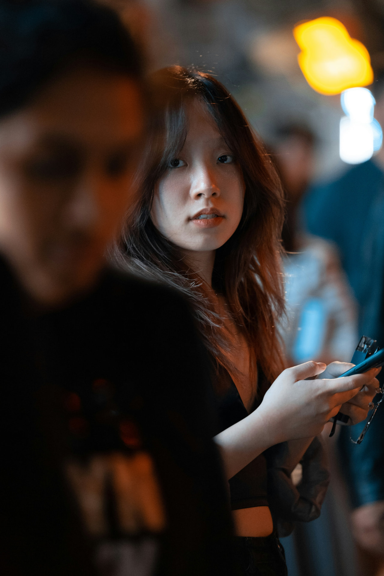 Young woman using her phone on a busy city street at night