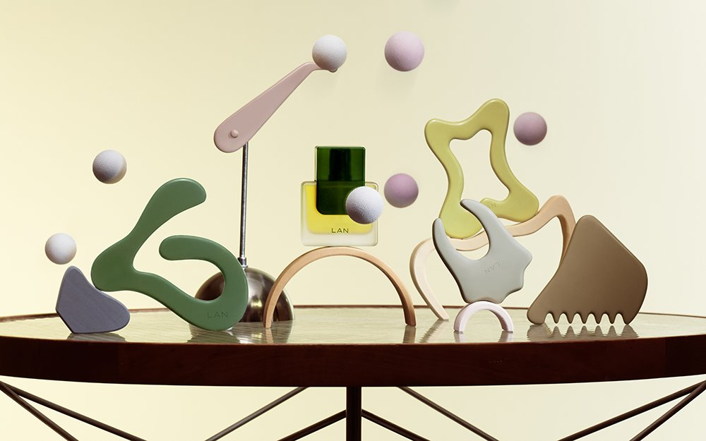 LAN skin yoga board set and serum bottle arranged with sculptural pastel objects on a table.