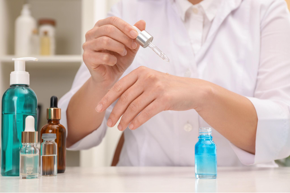 Lab technician testing a skincare serum with a dropper alongside formulation bottles