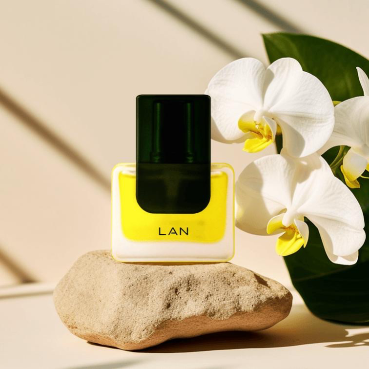 LAN clean skincare fragrance bottle on a stone beside white orchids