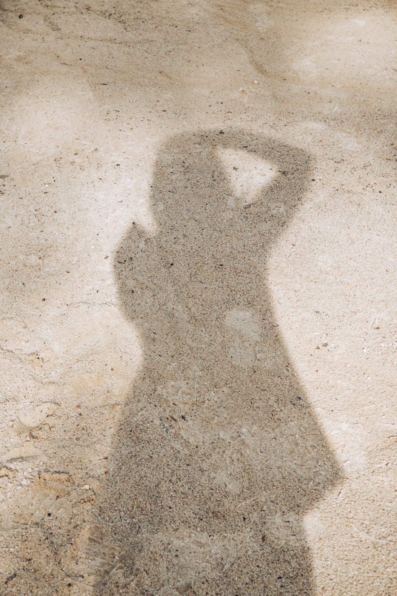 Shadow of a person holding up a phone cast on pale sand