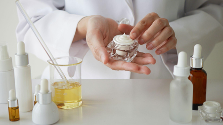 Cosmetics scientist holding a jar of cream beside laboratory glassware and serum bottles